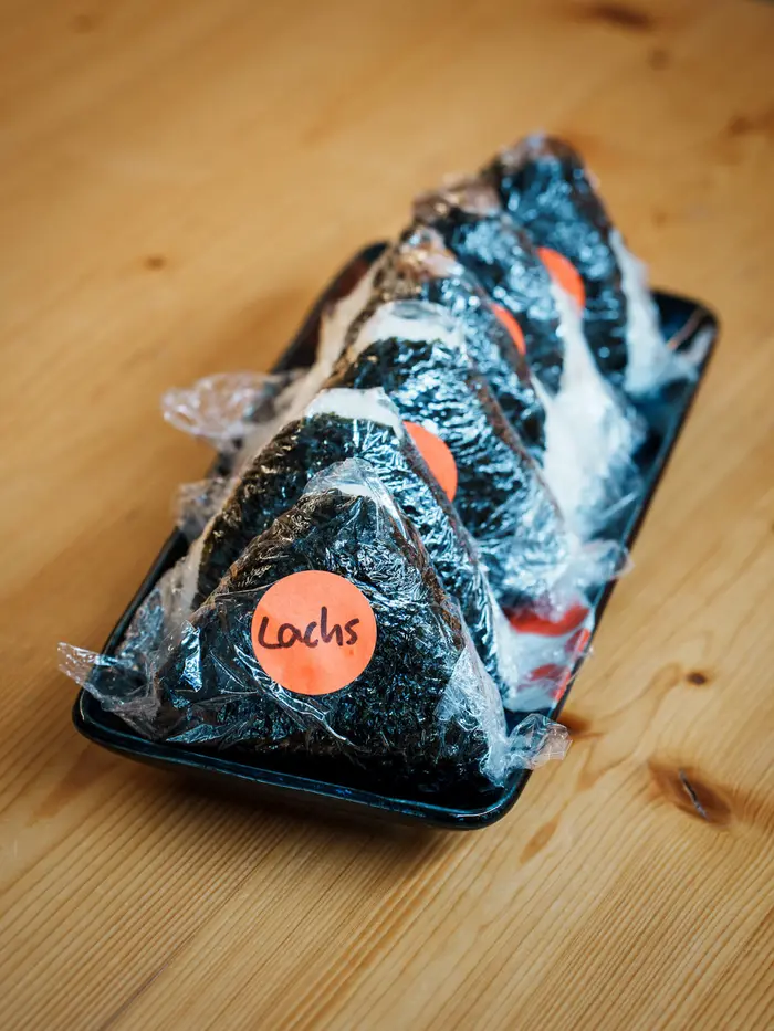 Lachs-Onigiri auf einem schwarzen Teller.